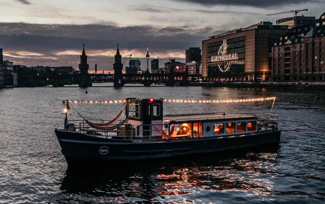 Illuminated party boat from Berlin Boat Rental on an evening boat tour on the Spree in front of the Oberbaum Bridge.