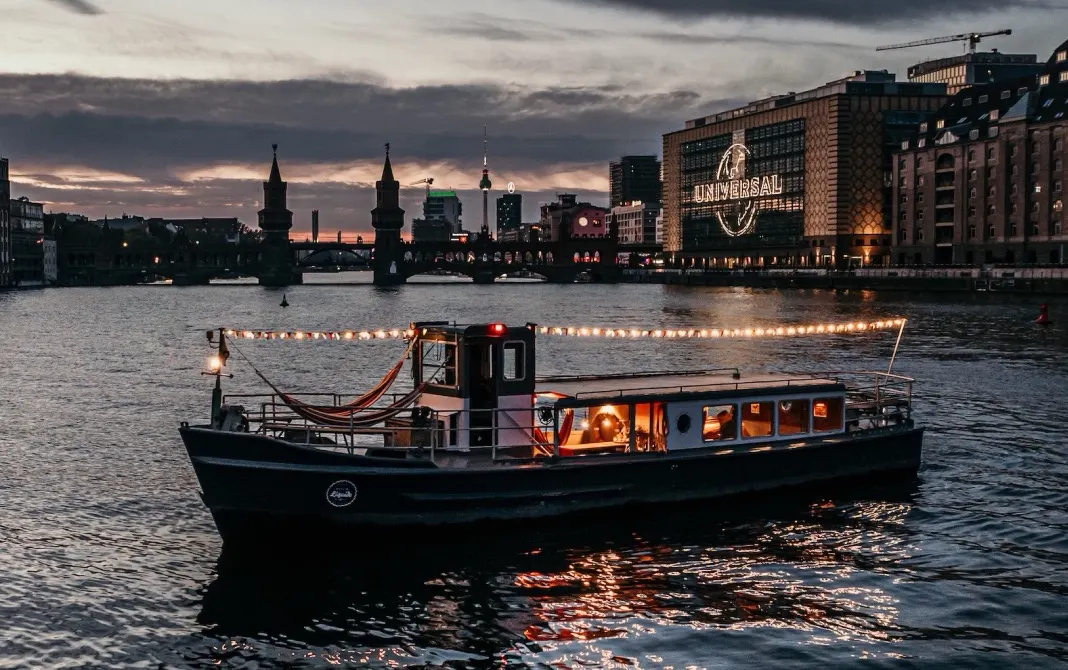 Illuminated party boat from Berlin Boat Rental on an evening boat tour on the Spree in front of the Oberbaum Bridge.