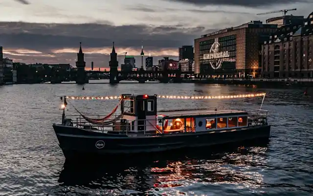 Illuminated party boat from Berlin Boat Rental on an evening boat tour on the Spree in front of the Oberbaum Bridge.